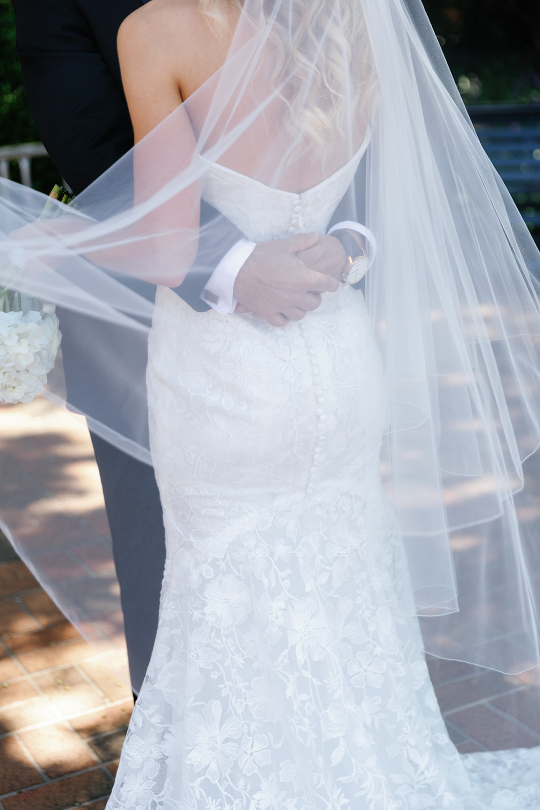 detailed shot of grooms arms wrapped around the bride's waits looking through the veil a moment taken during their wedding weekend timeline