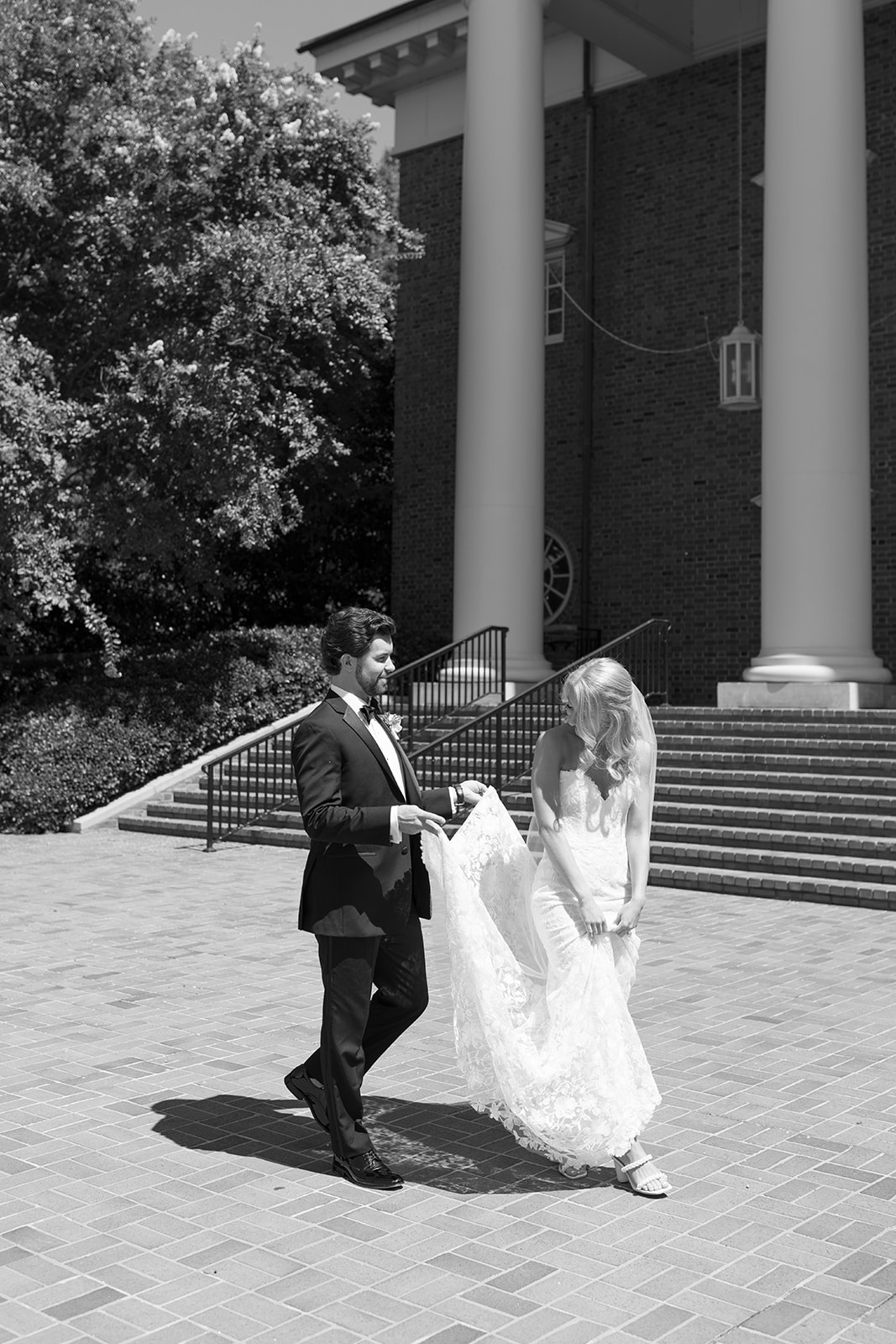 groom holding the bride's train as they walk 