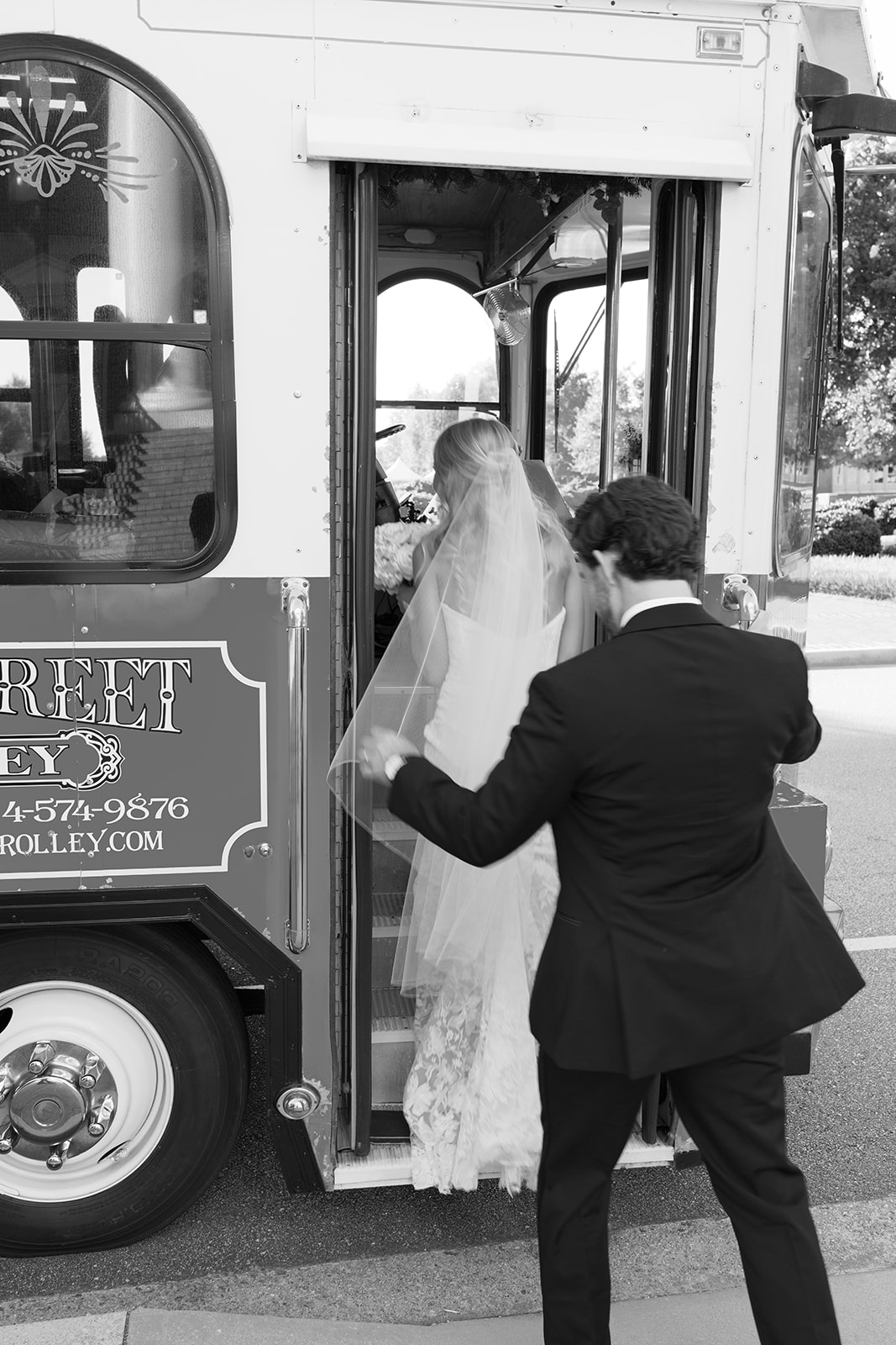 Groom helps bride onto a vintage trolley, her veil flowing behind her. A classic black-and-white wedding moment full of charm. Adding these fun moments in a Wedding Weekend Timeline allows you to have fun and enjoy the moment. 
