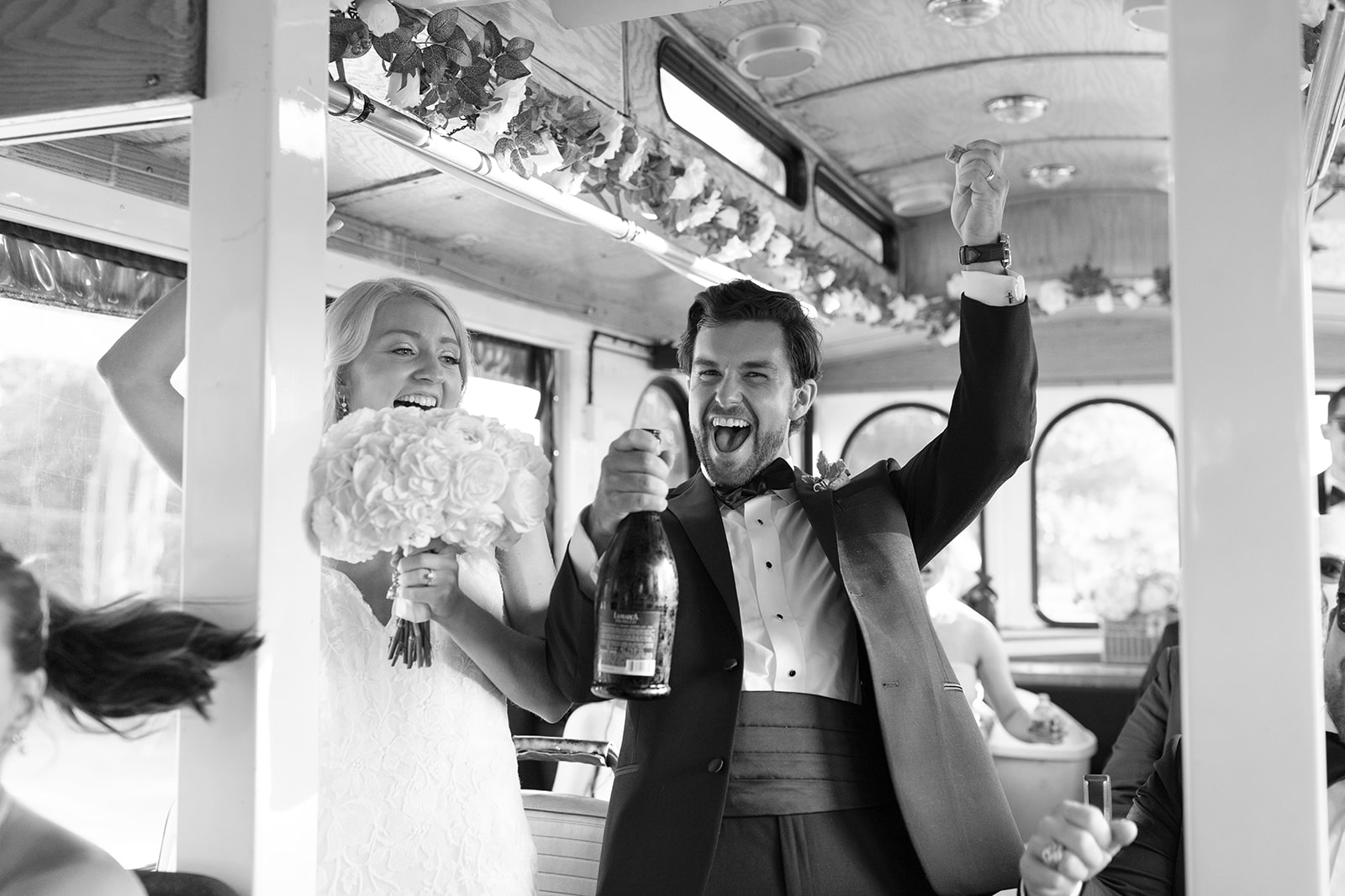 Groom pops champagne on a decorated trolley while the bride laughs beside him, holding her bouquet. A joyful moment in their Wedding Weekend Timeline!