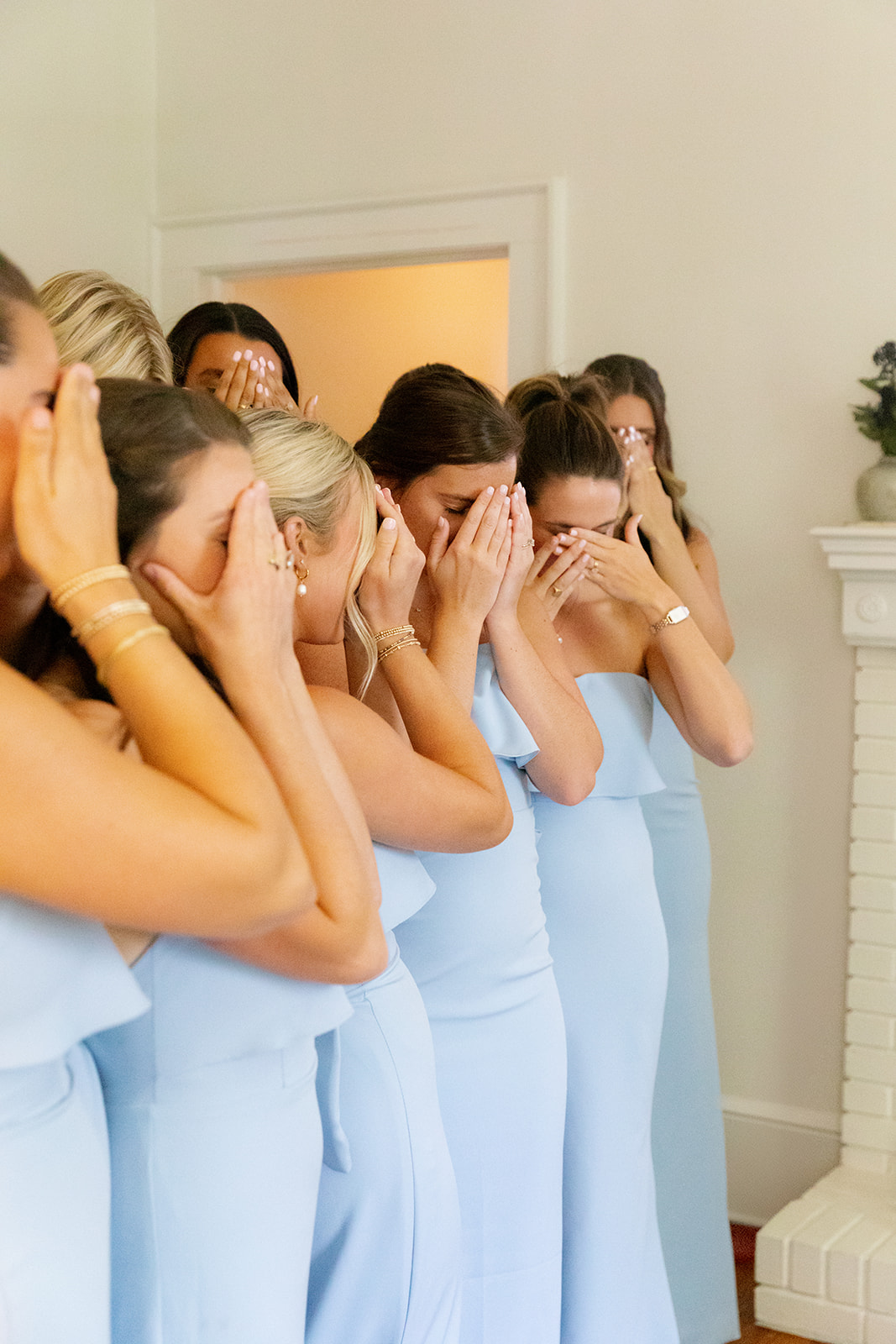 Bridesmaids in light blue dresses covering their eyes, waiting to see the bride for the first time