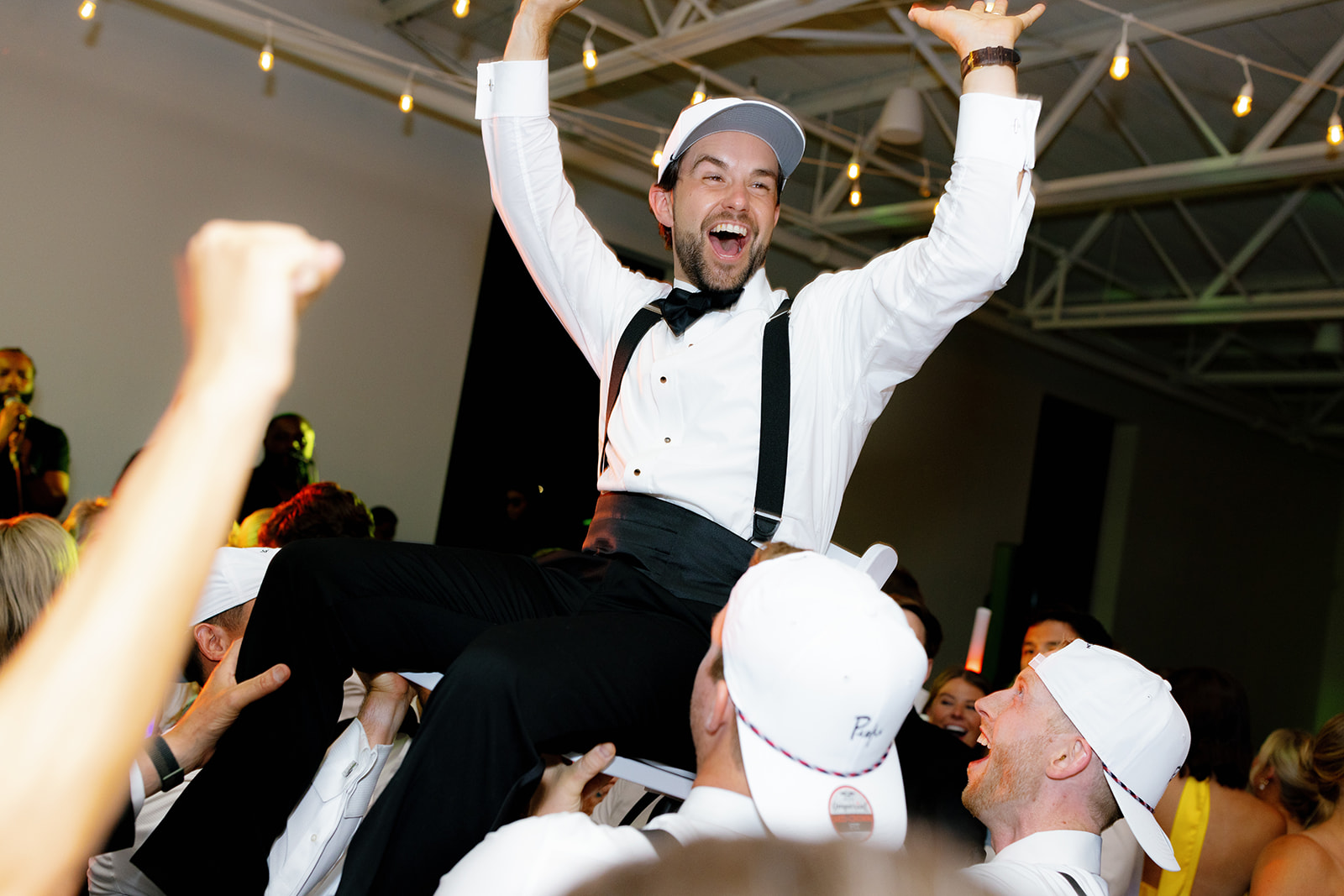 Groom hoisted into the air on a chair, smiling and raising his hands in excitement.