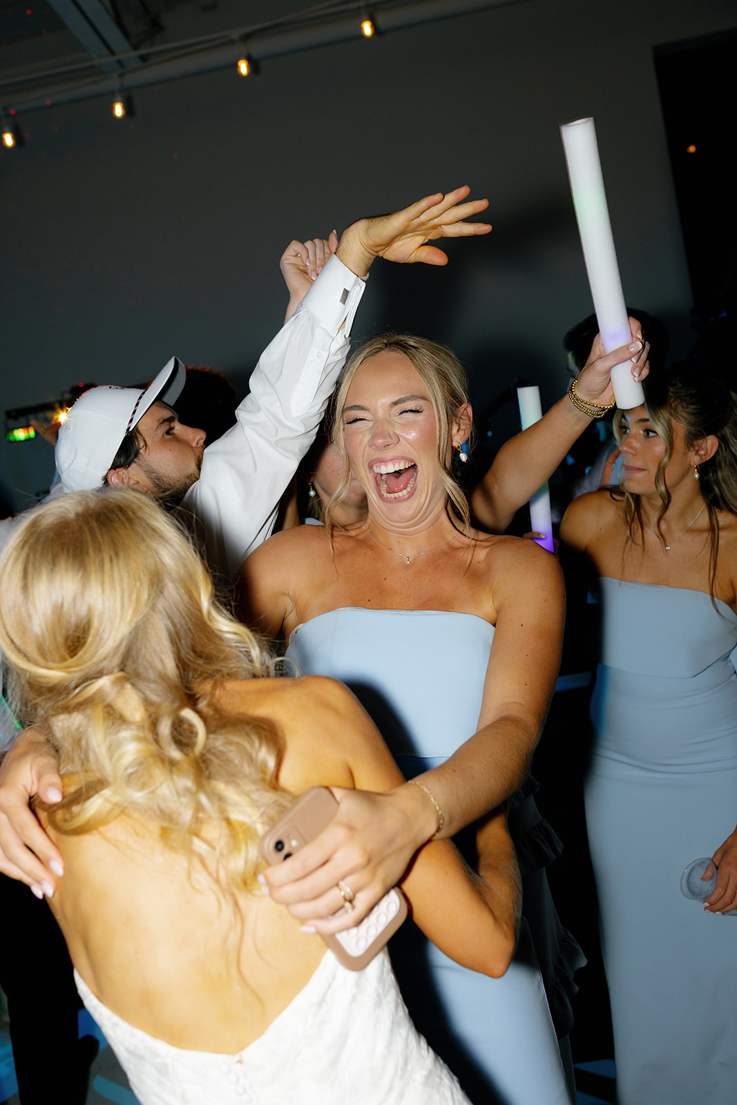 Bride dancing with a bridesmaid, both laughing and celebrating on the packed dance floor.