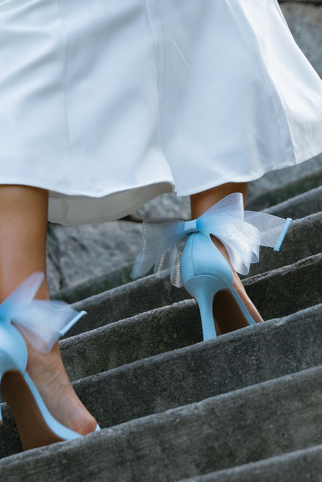Bride walking up stone stairs in light blue bow heels, a stylish 'something blue' wedding detail.