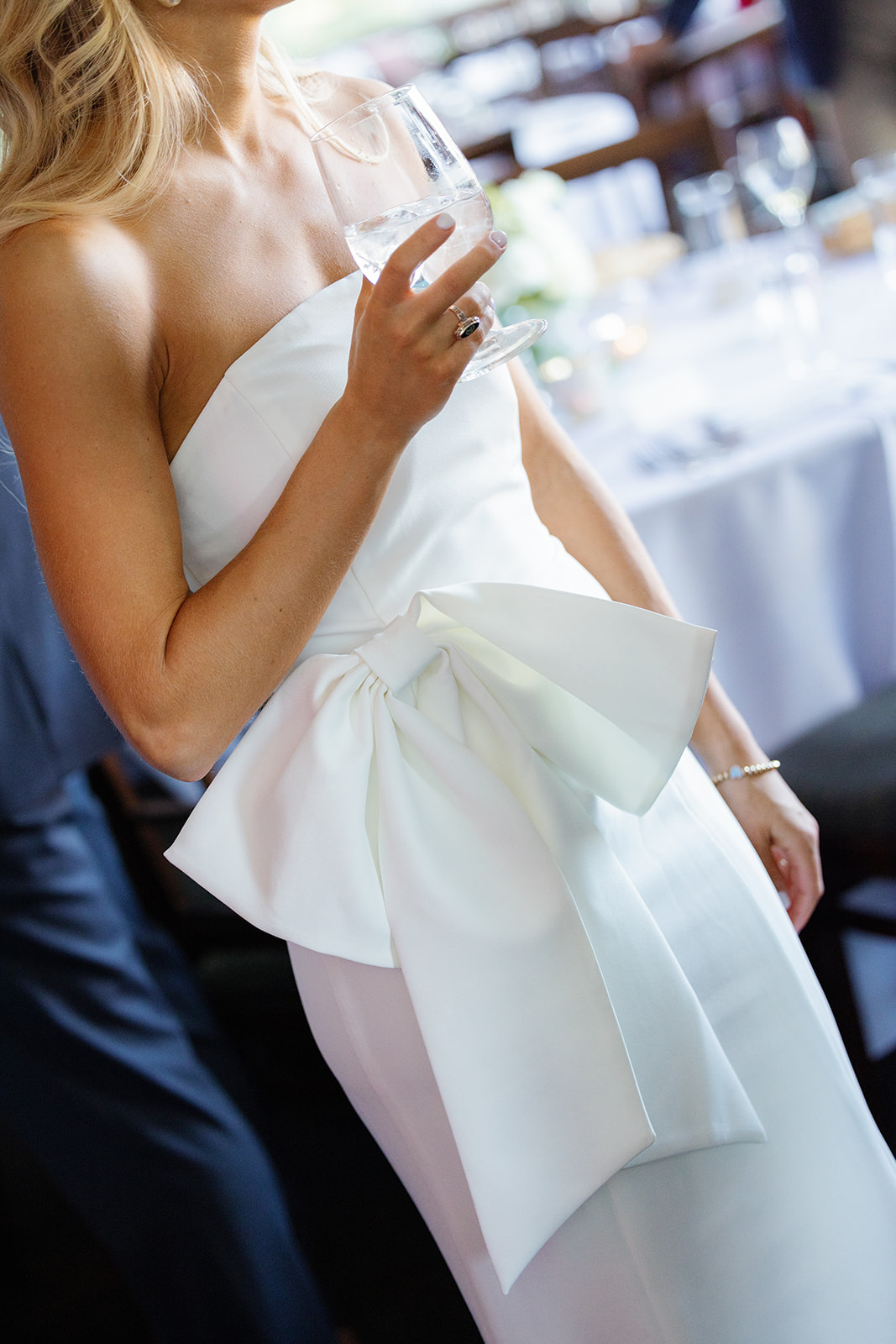 Bride in a strapless white dress with a statement bow detail, holding a glass at her Greenville, SC rehearsal dinner.
