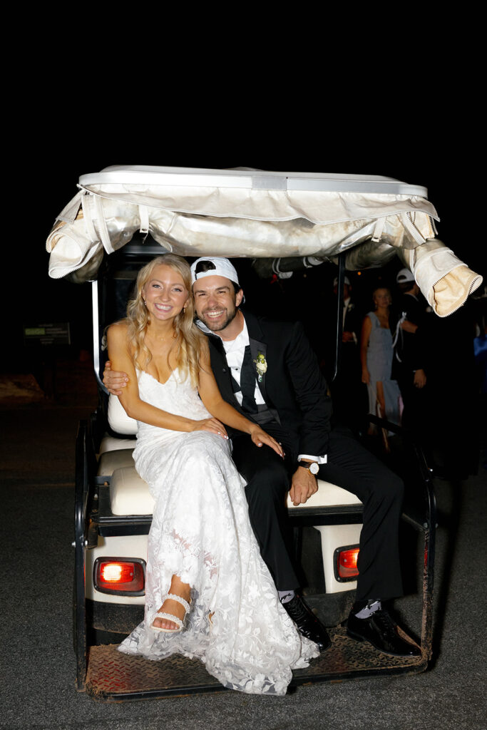 bride and groom pose on golf cart for the the final detail of their wedding weekend timeline