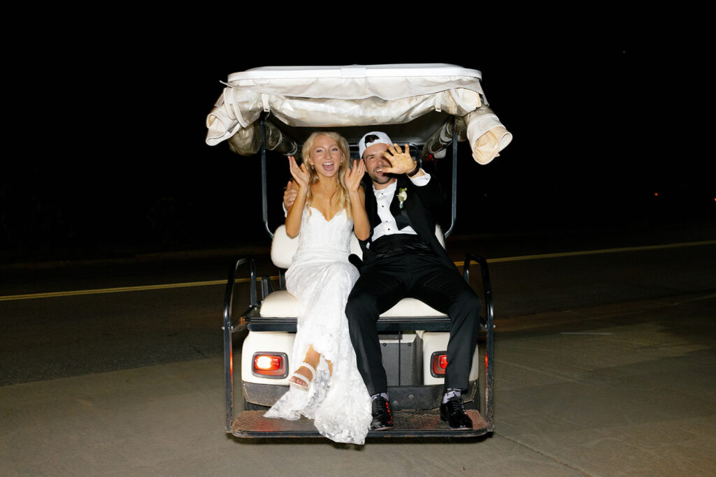 bride groom sit on gold cart and wave goodbye to guests for the the final detail of their wedding weekend timeline