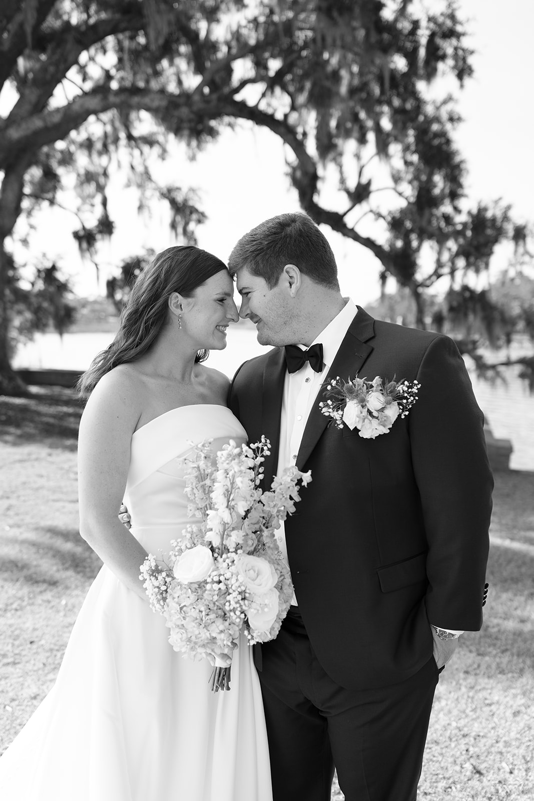 The couple shares a quiet moment with foreheads touching beneath the mossy trees by the water.