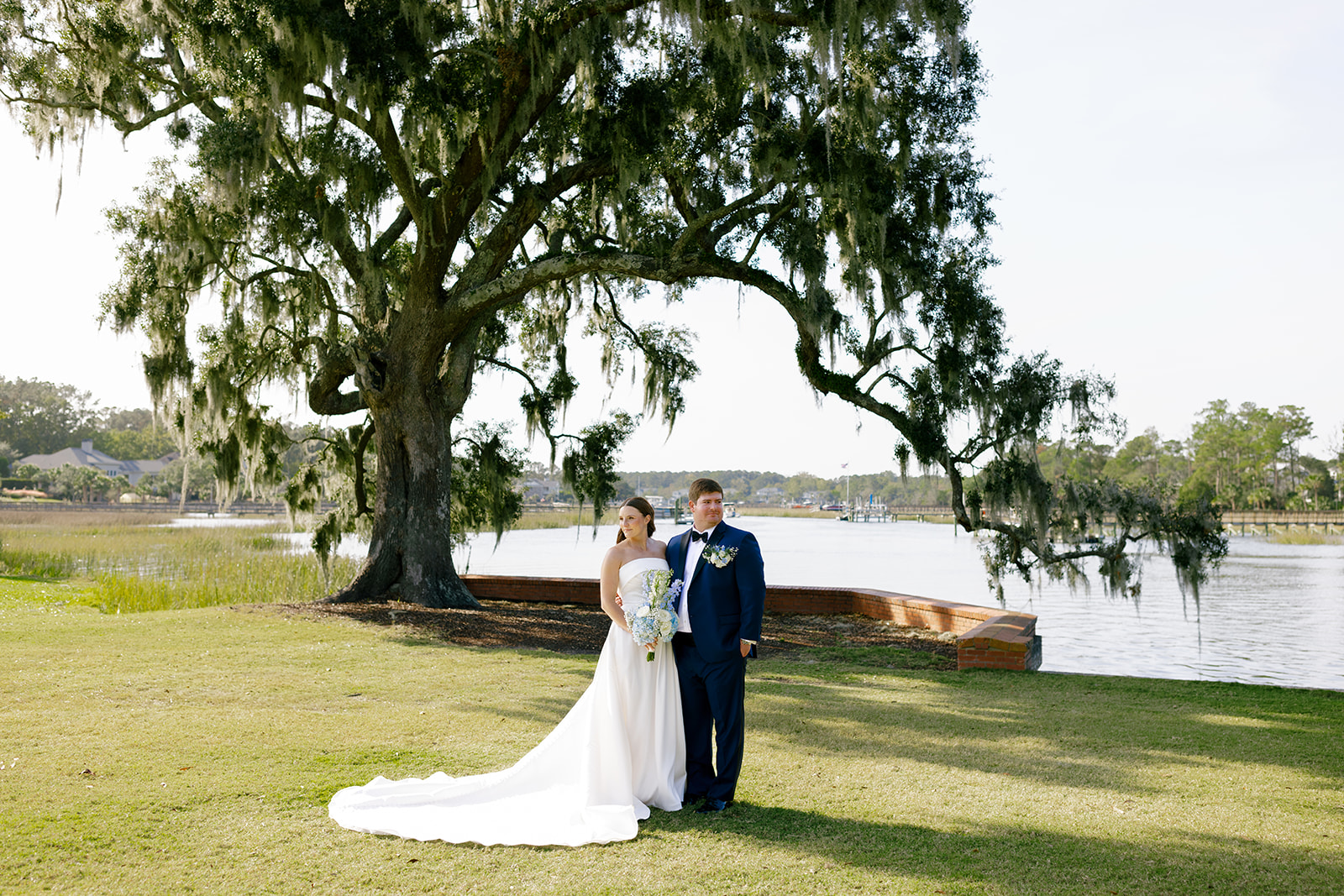 bride and groom portrait with a big tree and water behind them 