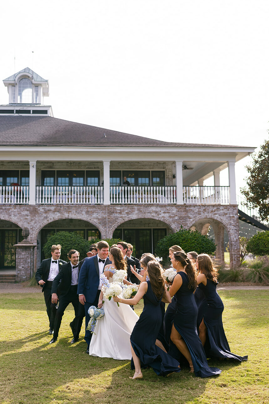 Wedding party cheers around the couple outside the clubhouse at Dunes West.