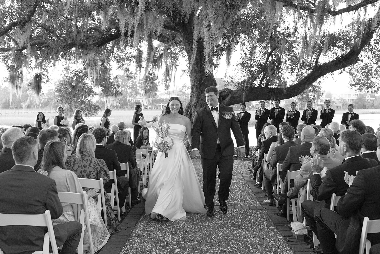Bride and groom walk hand in hand down the aisle as guests cheer at their waterfront South Carolina ceremony.
