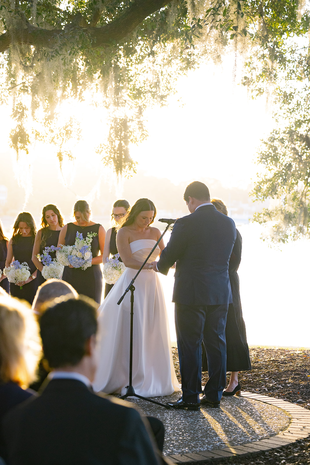 Groom places a ring on the bride’s finger during their waterfront wedding vows under golden light.