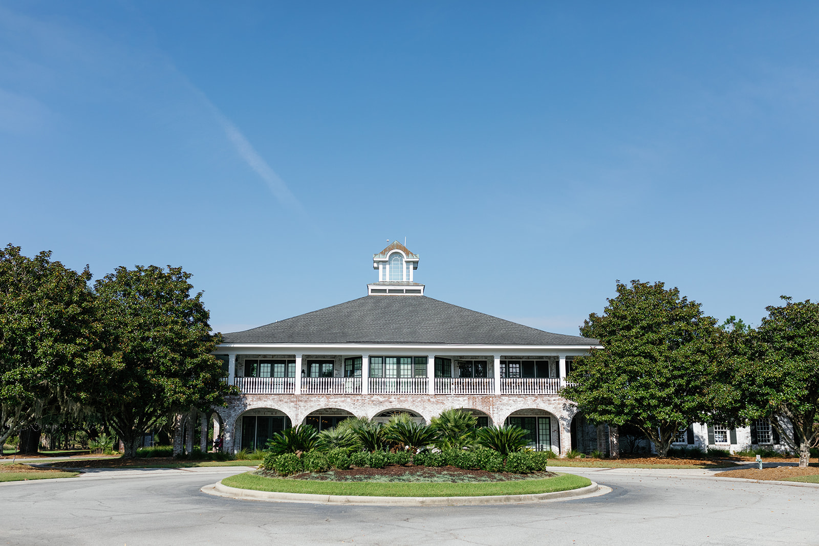 Exterior of Dunes West Golf & River Club on a sunny day, framed by palm trees and brick arches.