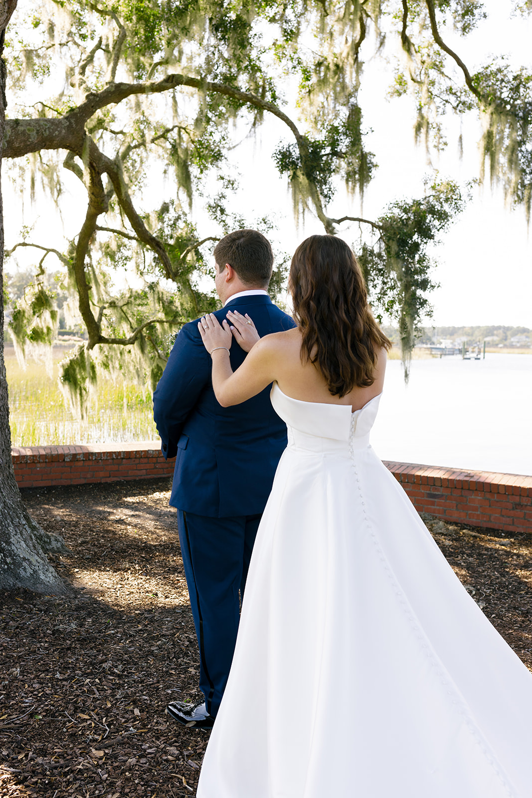 Mills gently places her hands on Brooks’ shoulders during their first look beneath mossy oak trees.