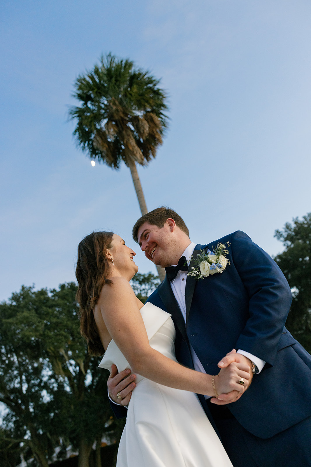 bride and groom smiling at each other with a palm tree towering above them