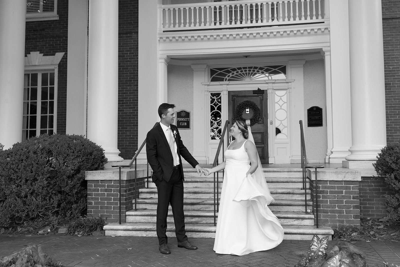 Newlyweds pause to hold hands and smile at each other outside the stately front entrance of the Poinsett Club taken by a Greenville wedding photographer.