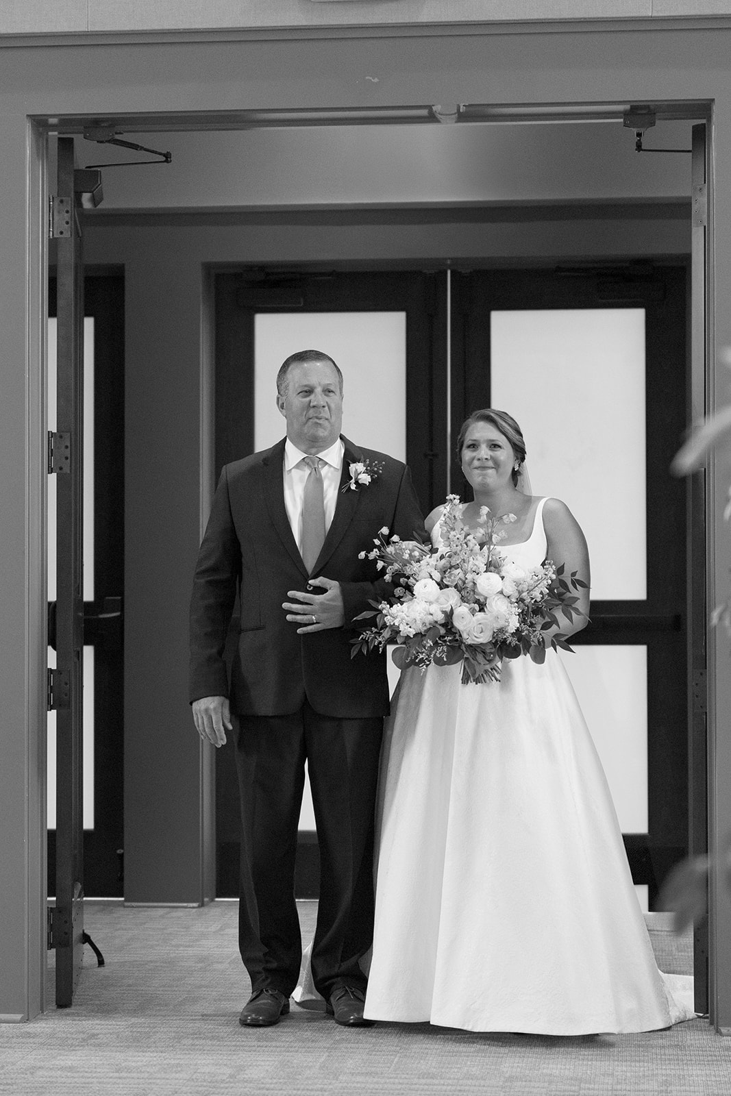 Bride stands arm-in-arm with her father at the church entrance, bouquet in hand, ready for the ceremony.