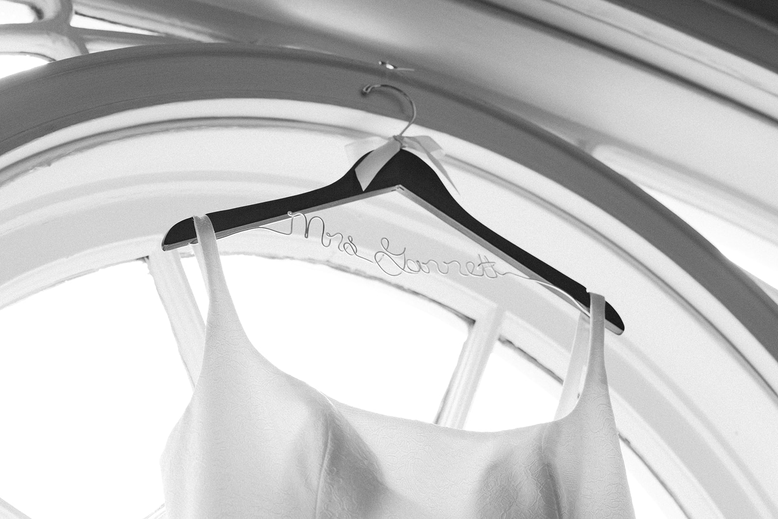Close-up of custom wire hanger reading “Mrs. Garrett” holding the bride’s timeless ivory gown.