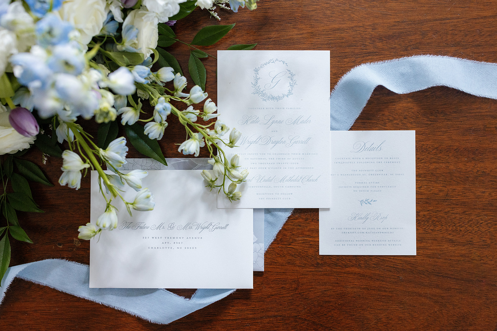 Romantic flat lay of Katie and Wright’s invitation suite surrounded by soft blooms and powder blue ribbon.