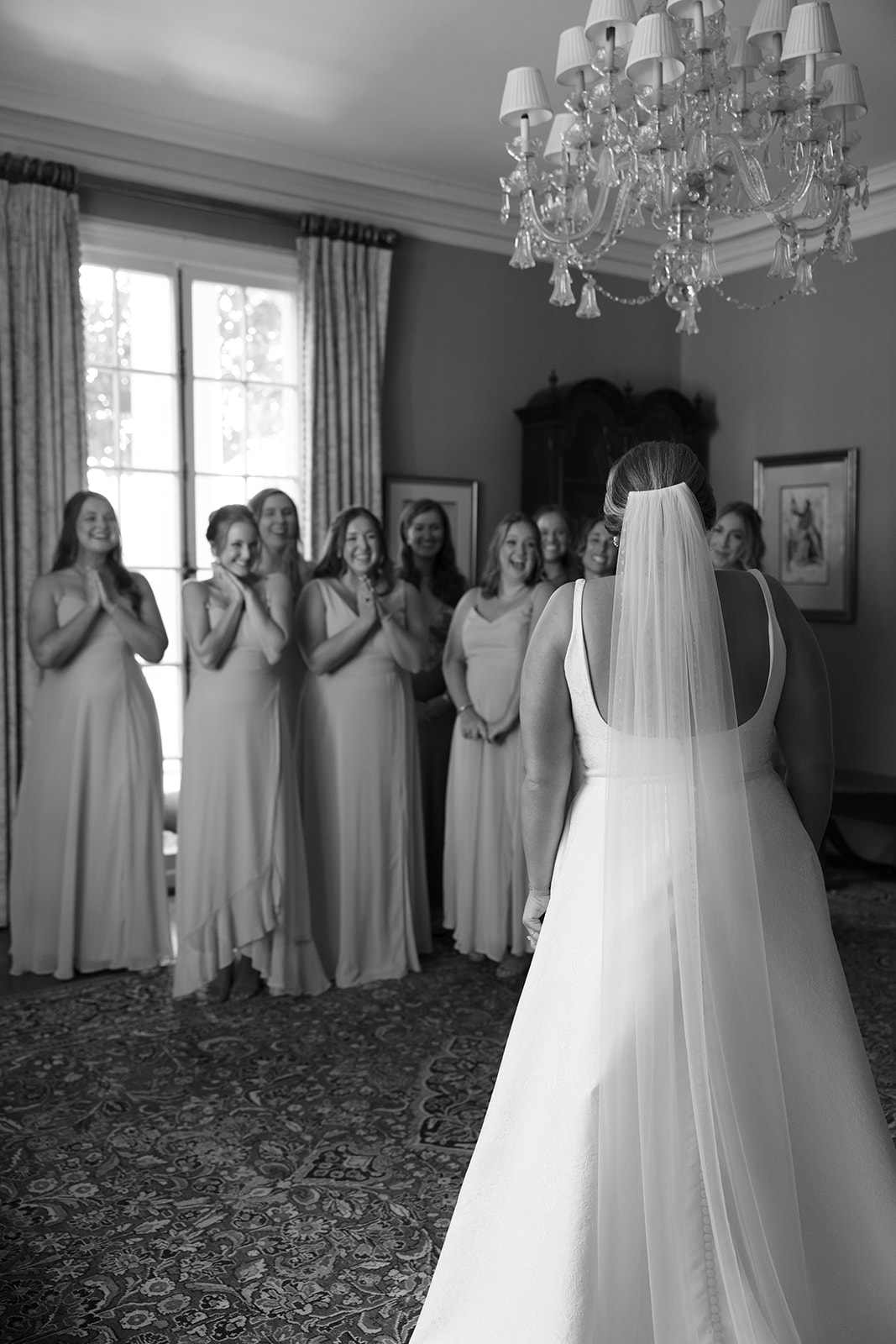 black and white of bridesmaids react with joy as the bride reveals her dress during an emotional first look.