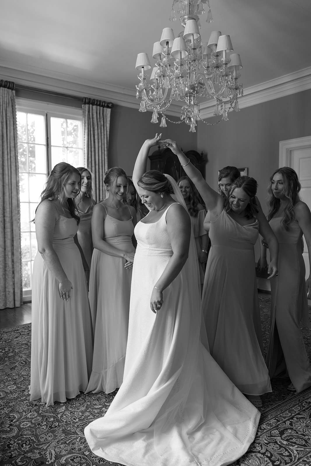 Bridesmaids spin the bride playfully in her gown under a sparkling chandelier taken by a Greenville wedding photographer.