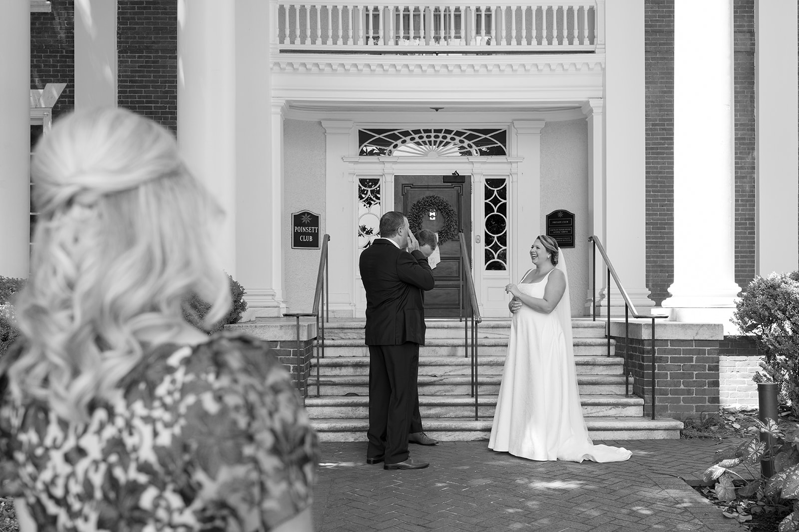 Bride shares a joyful greeting with family members at the entrance of the Poinsett Club taken by a Greenville wedding photographer.