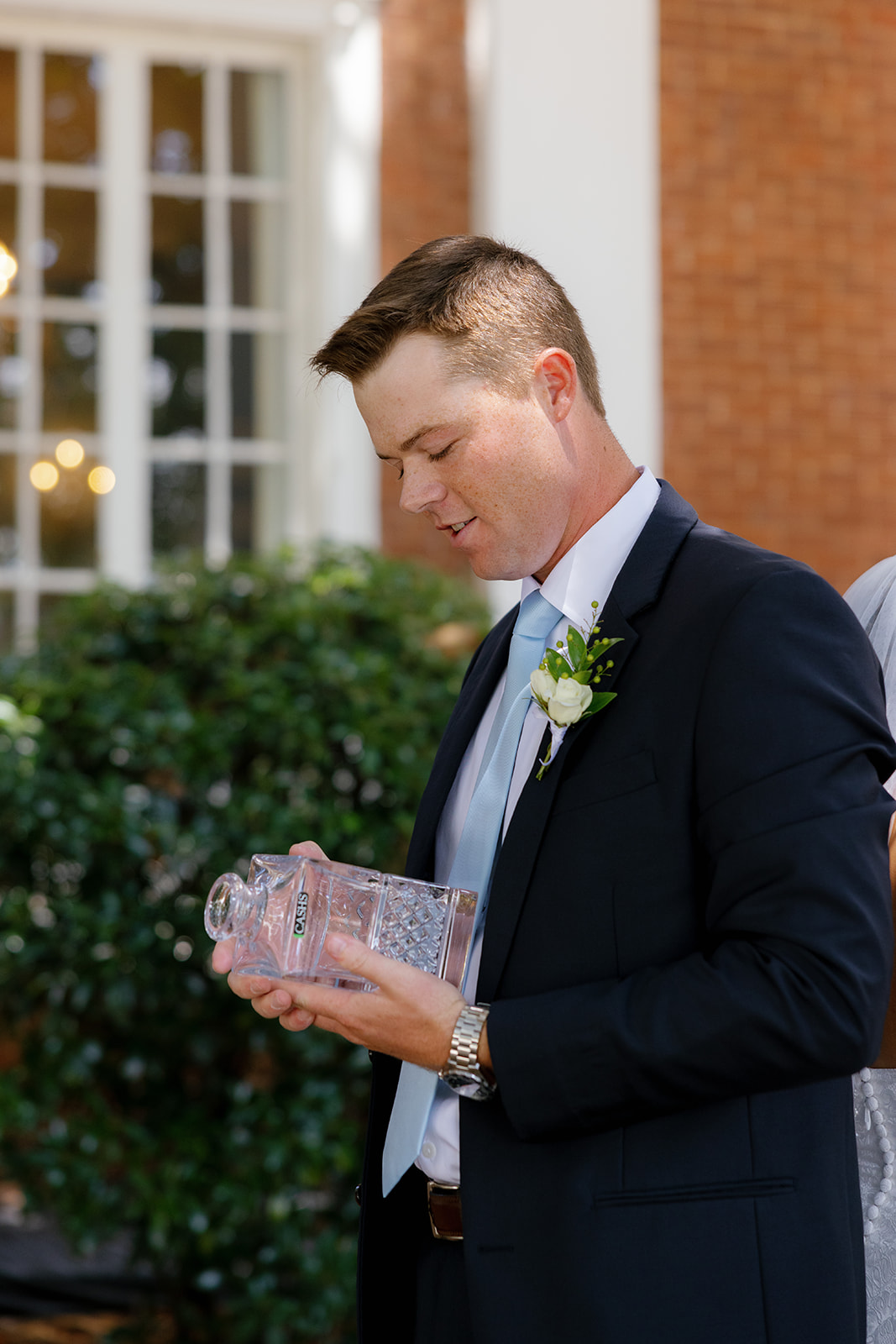 Groom admires a personalized crystal decanter gifted by the bride on their wedding day taken by a Greenville wedding photographer.