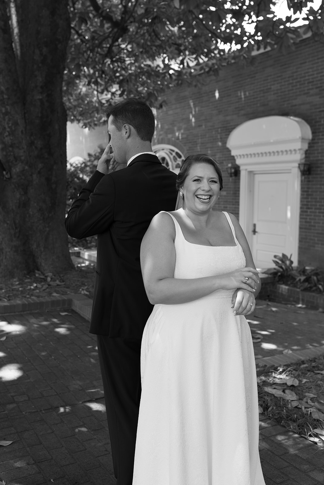 Bride and groom back to back during a joyful first touch outside a brick venue.