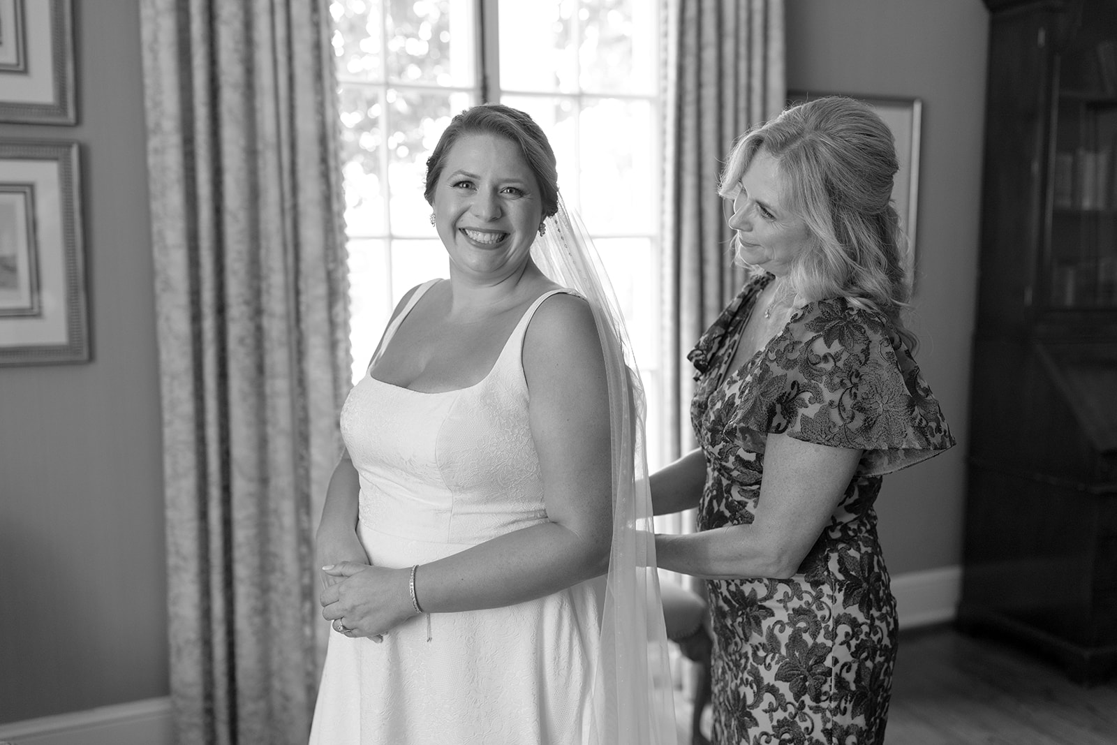 bride beams while her mom helps with her wedding dress in a sweet pre-ceremony moment.