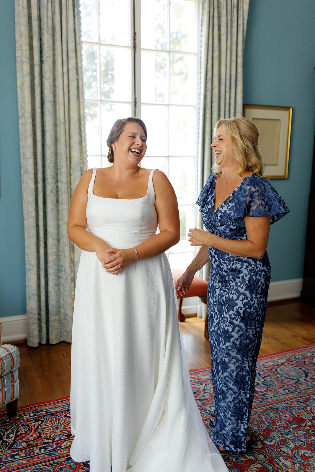 Bride and mother share a joyful laugh together while finishing final touches before the ceremony.