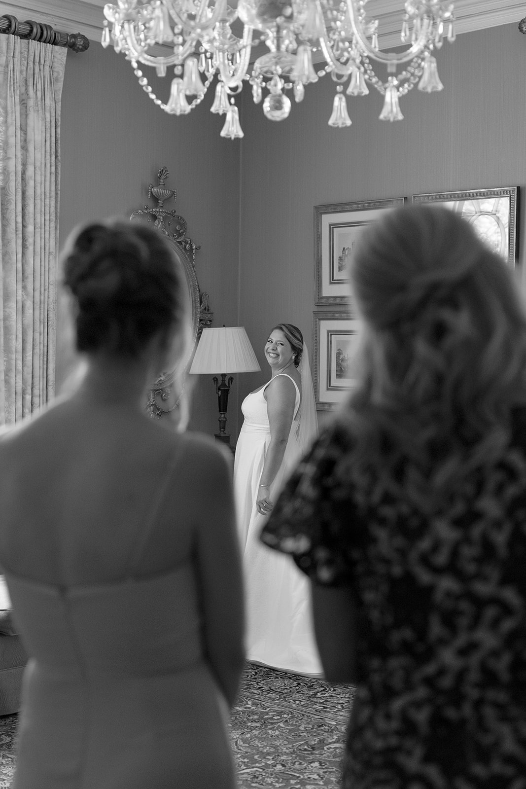 The bride turns to show her gown, beaming at her bridal party in an emotional black and white moment.
