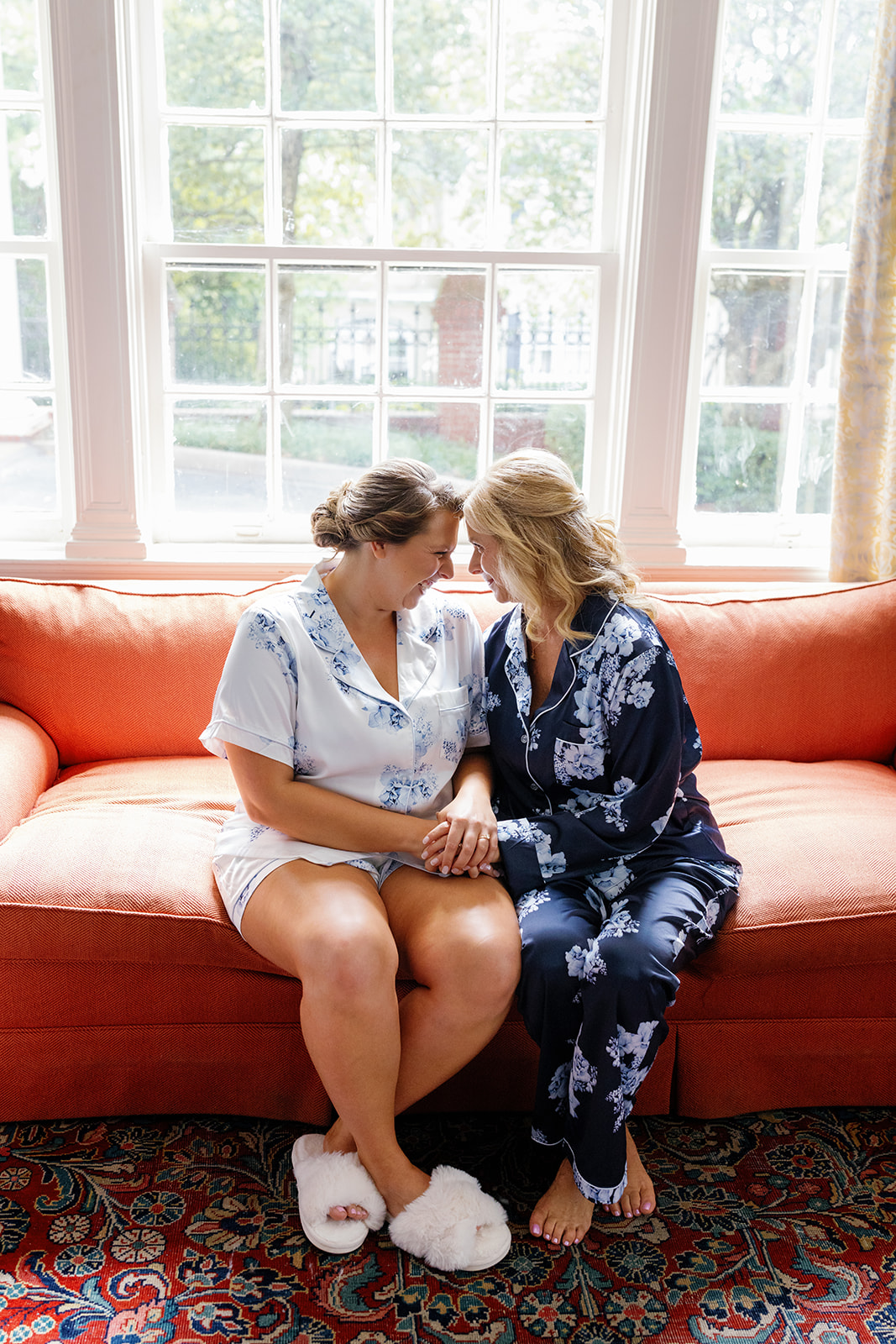 Bride and her mom sit forehead to forehead in matching pajamas, sharing a quiet, tender moment.