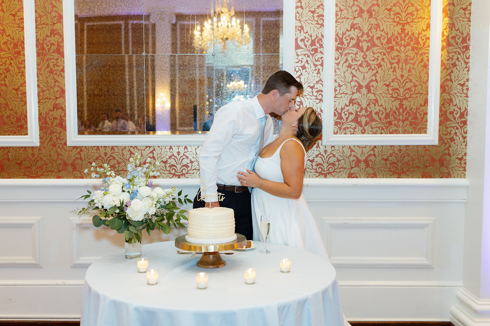 The pair shares a sweet kiss next to their elegant white cake with floral accents and candlelight taken by a Greenville wedding photographer.