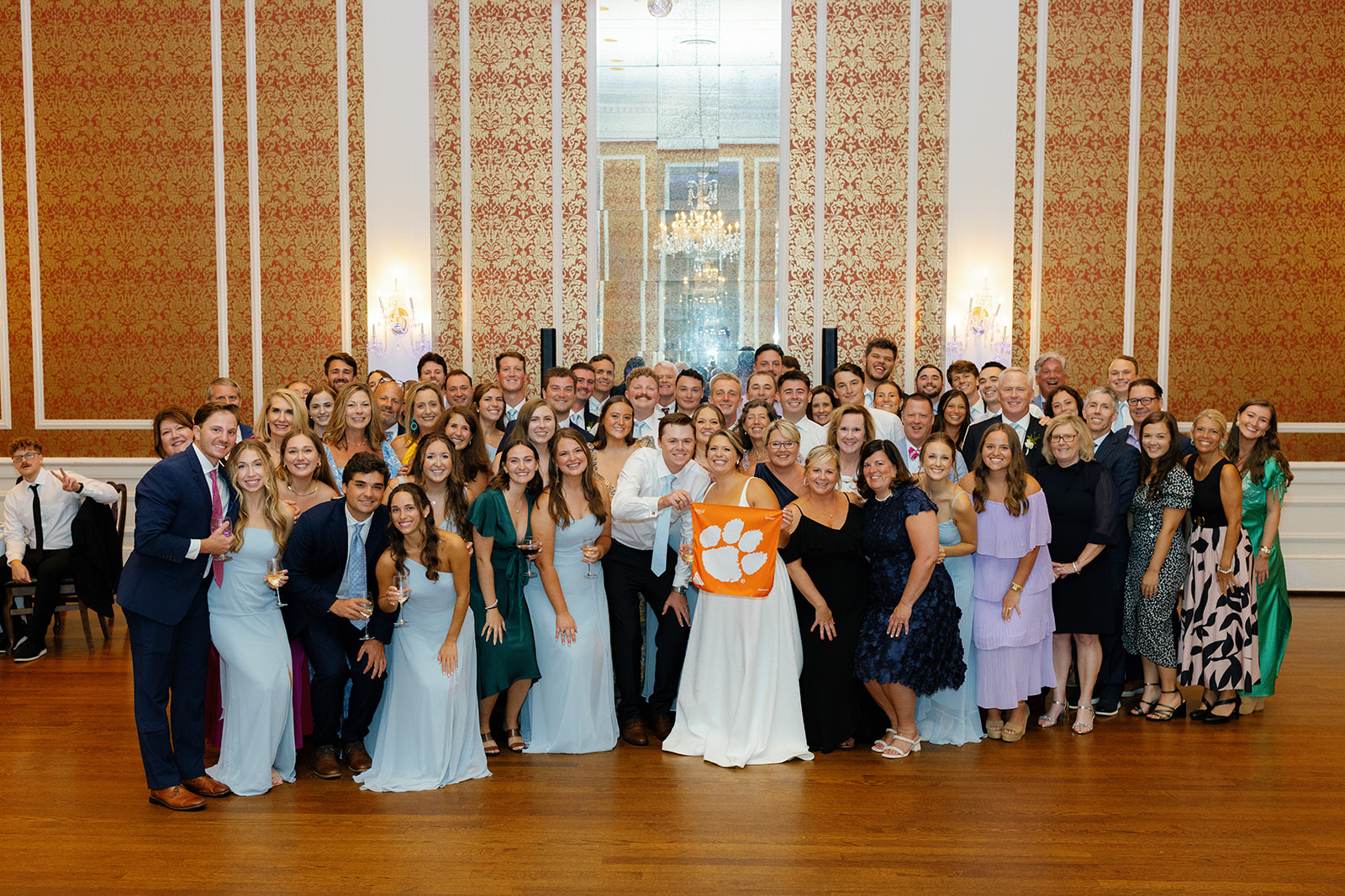 bride and groom pose with their wedding guests holding a Clemson flag