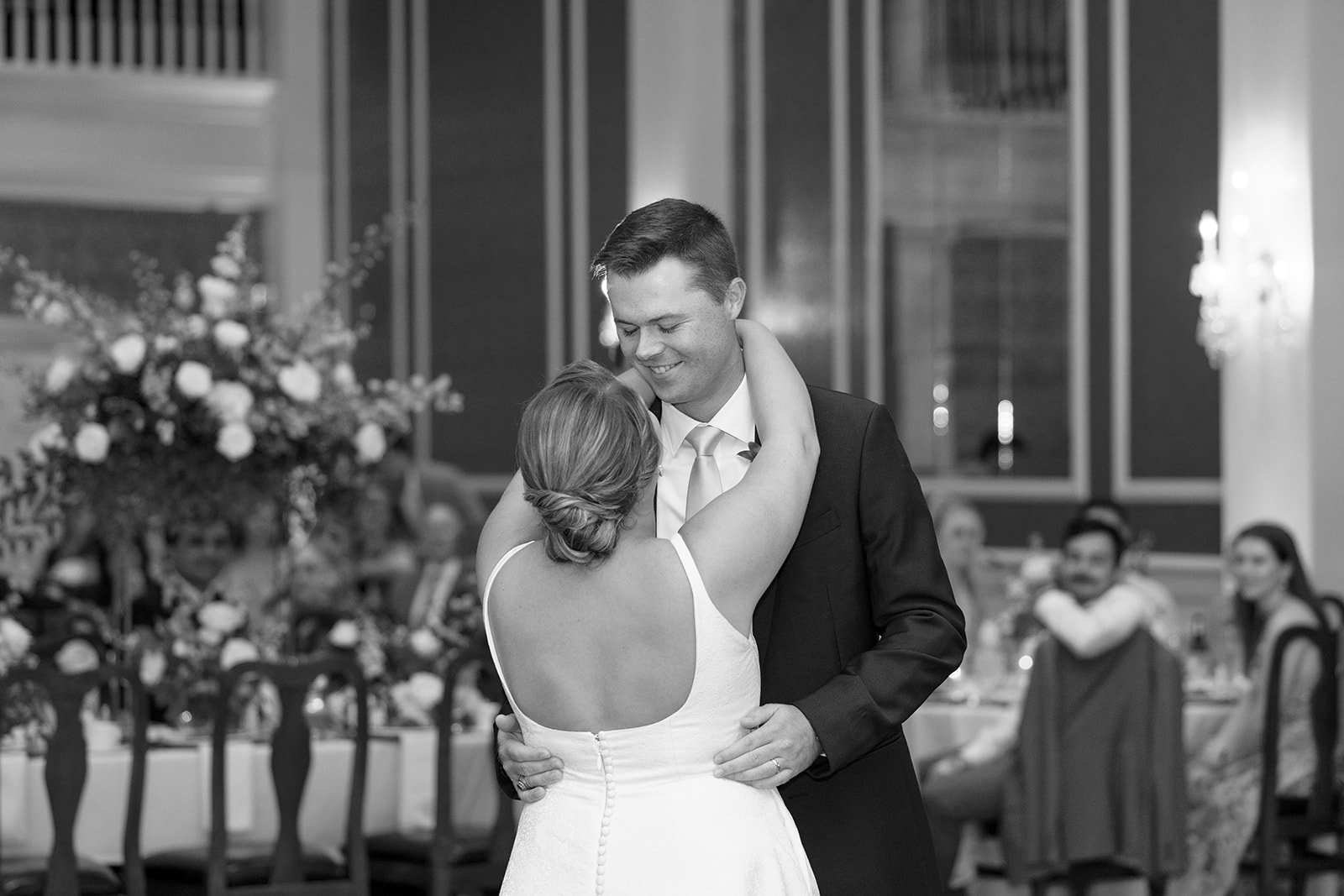 Newlyweds share their first dance, smiling tenderly in the softly lit reception space.