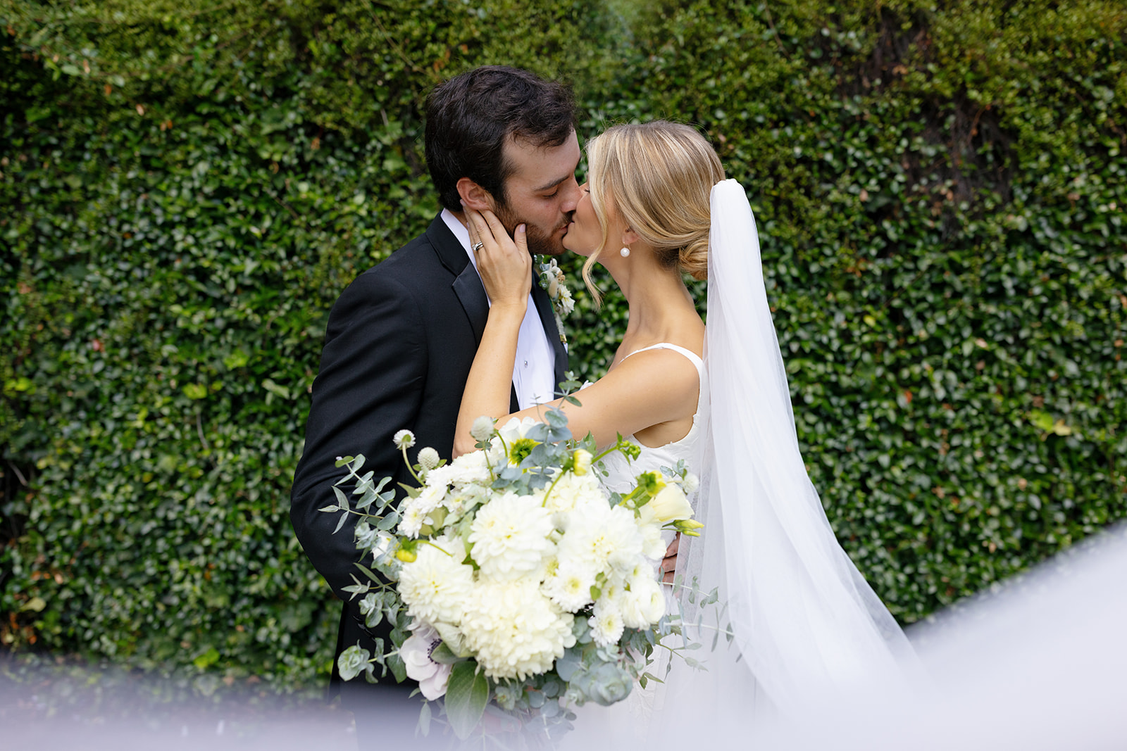 Bride and groom share a romantic kiss, framed by her elegant white bouquet.