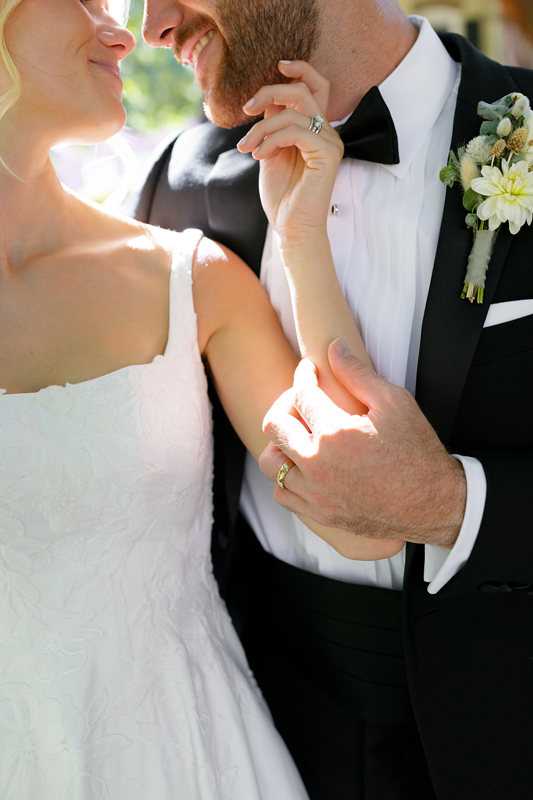 Close-up of bride and groom smiling as they hold hands, showcasing their wedding rings and joyful connection.