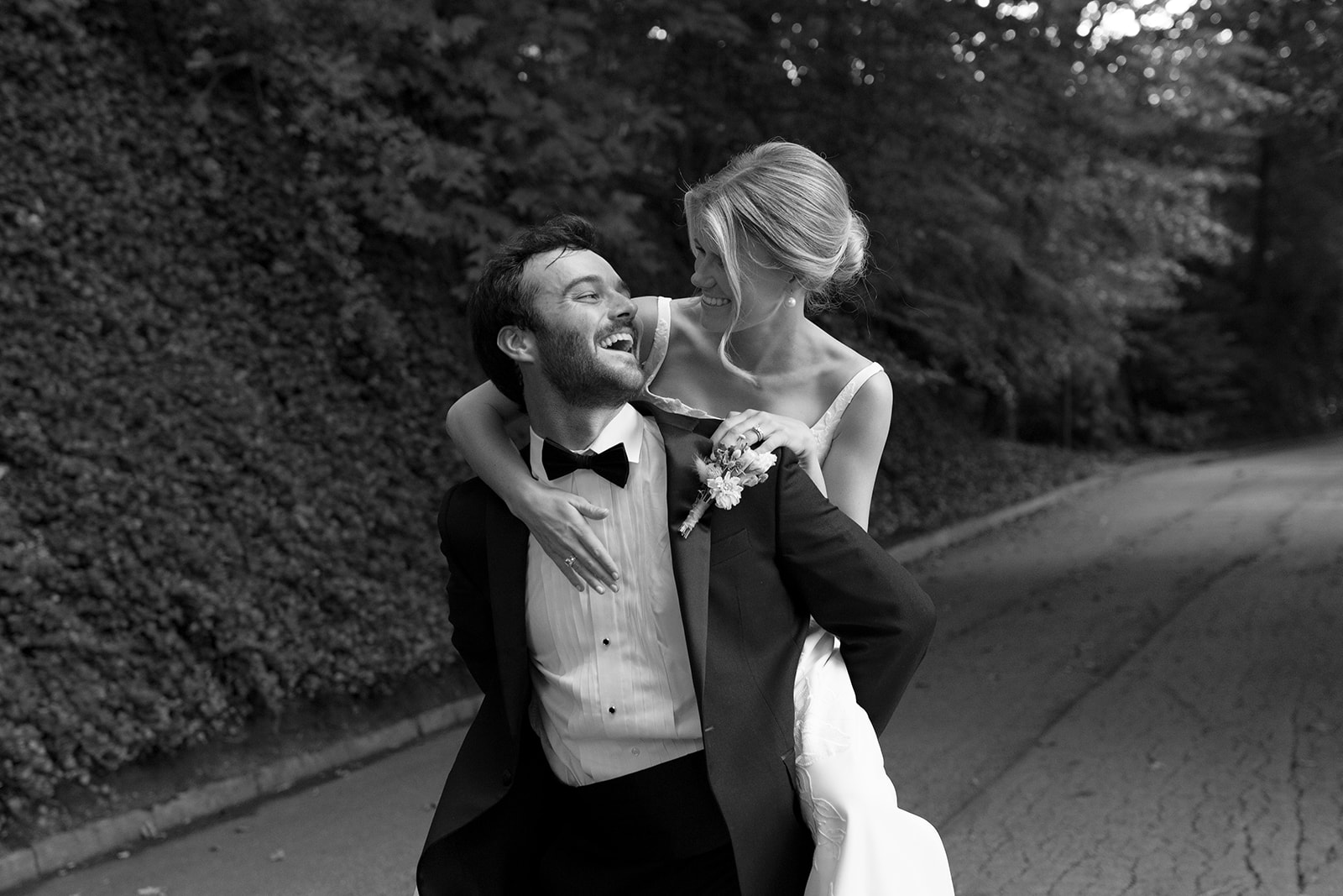Bride rides on groom’s back as they laugh together on a wooded path, full of joy.