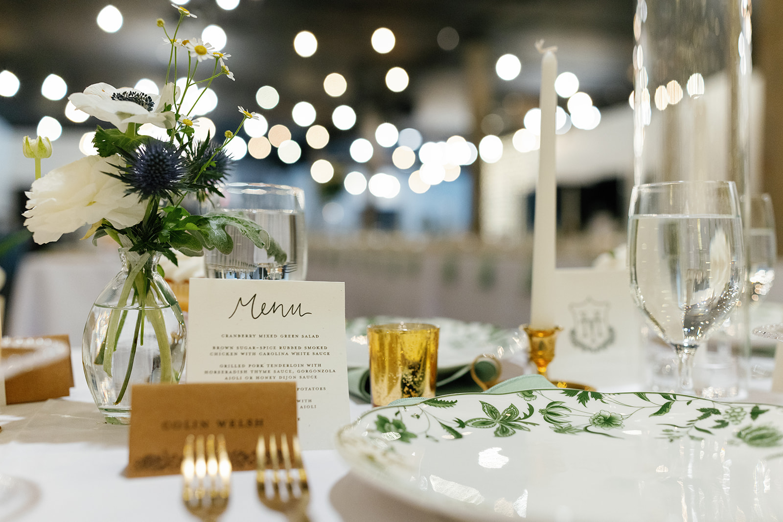 Close-up of a floral centerpiece, menu card, and candlelight on a softly lit reception table.