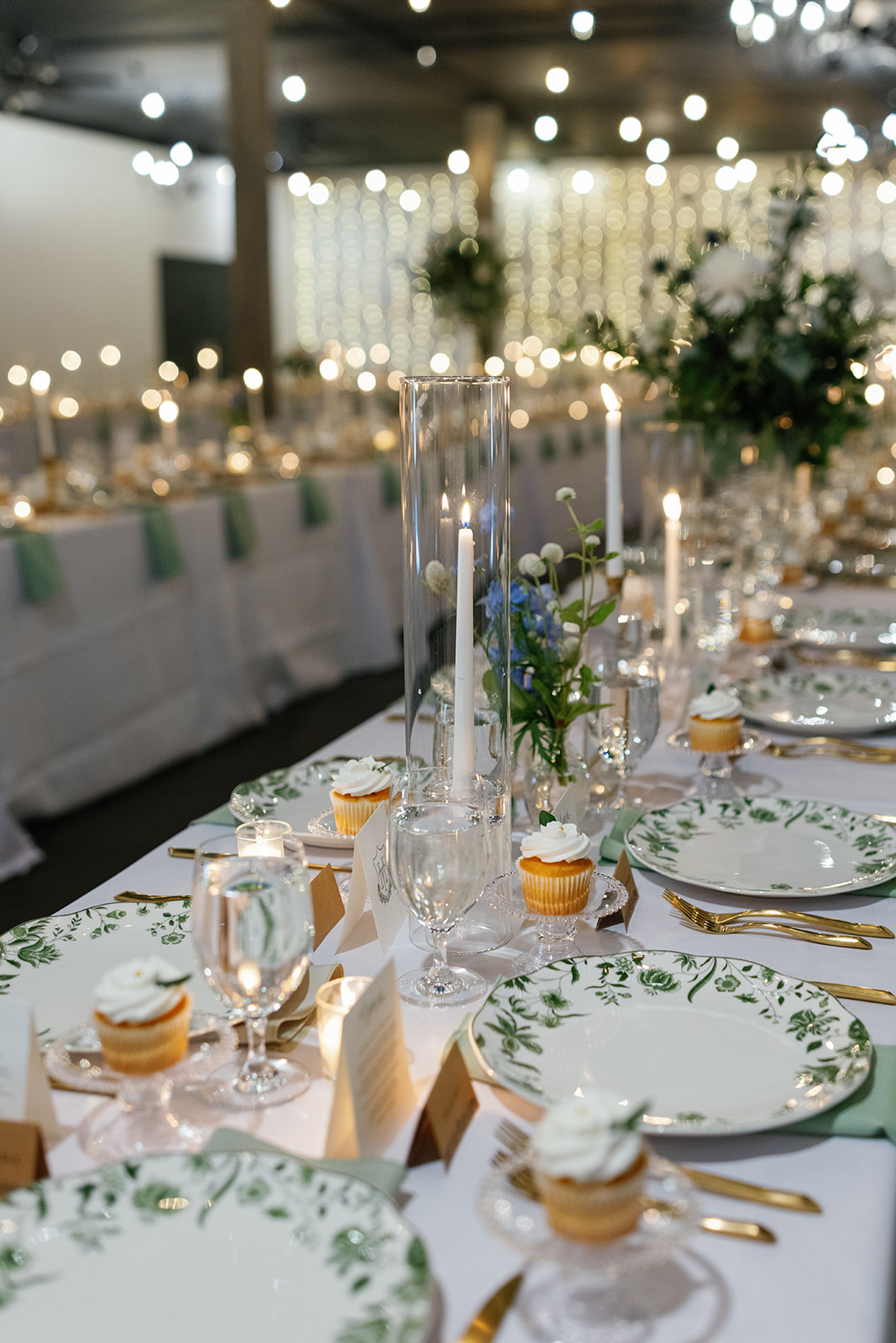 Elegant reception tables set with floral china, candlelight, and cupcakes for a romantic dinner.
