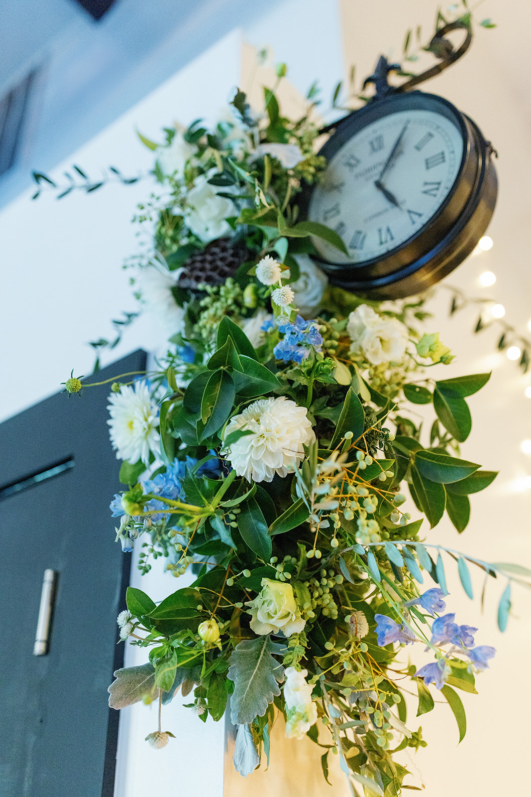 Romantic greenery and florals surround a vintage-style clock inside Vue 1919’s elegant venue space.