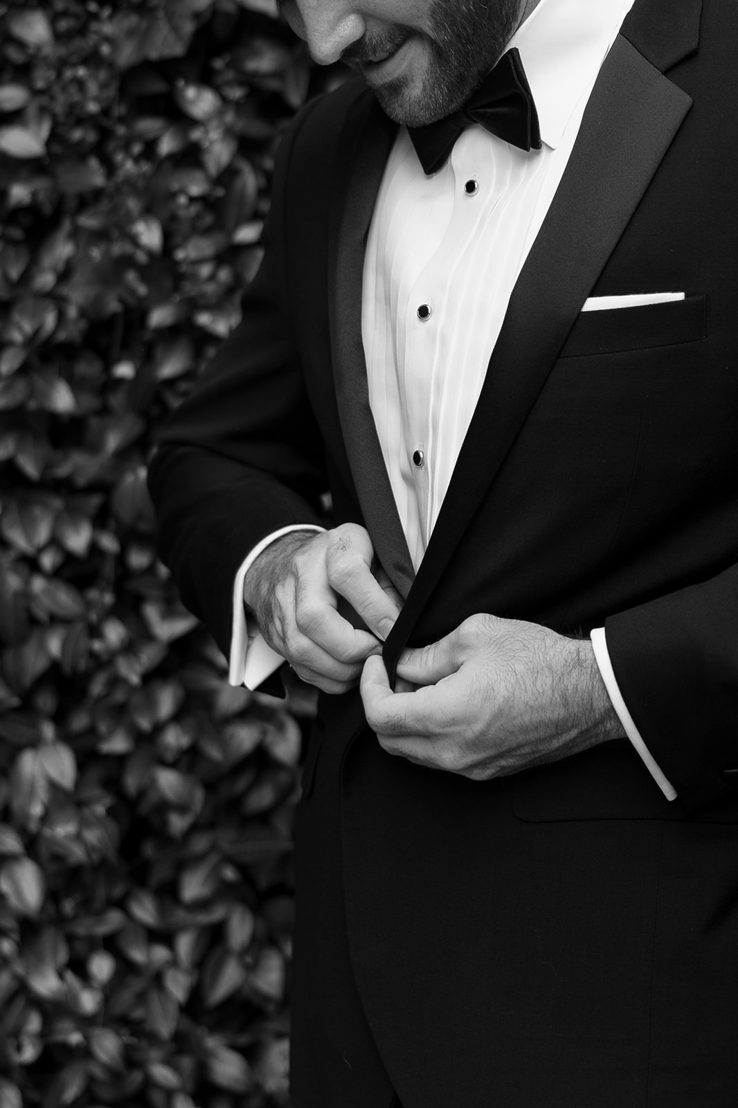 Groom buttons his tuxedo jacket in a timeless black-and-white portrait before the ceremony.