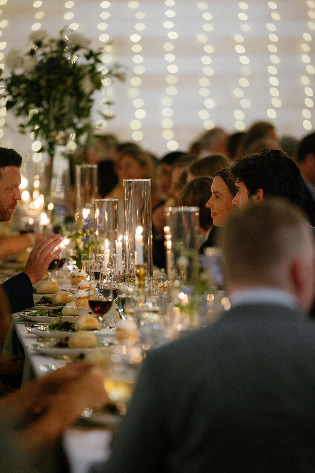 Guests dine by candlelight under string lights during a cozy and elegant wedding dinner.