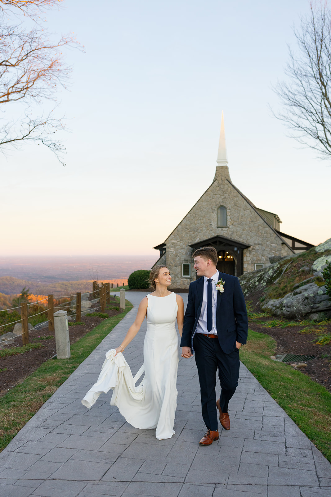 Bride and groom gaze at each other lovingly as they walk on the glassy chapel path at golden hour.