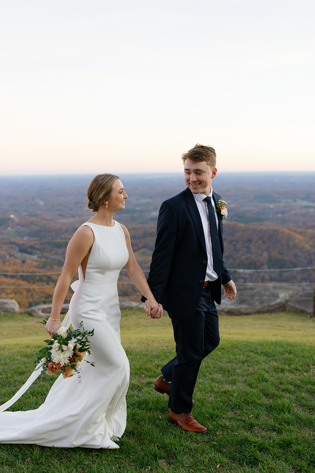 newlyweds smile at each other as they walk across the lawn at the Cliffs at glassy chapel