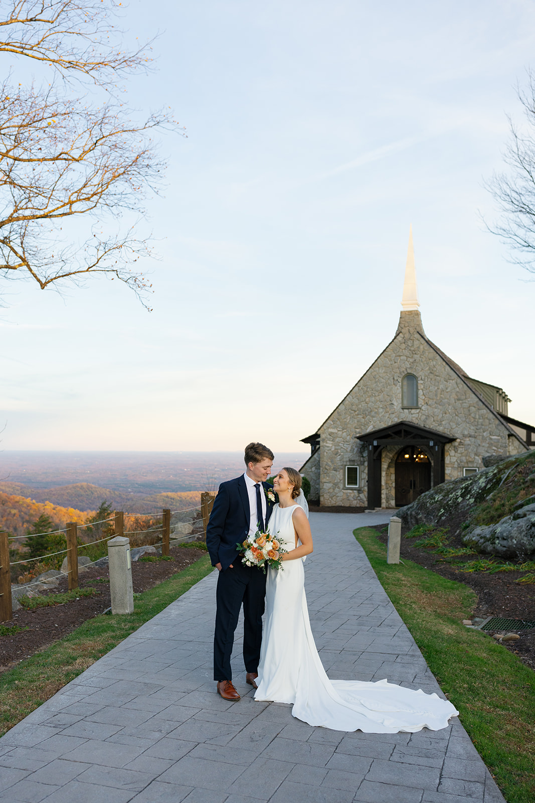 Bride and groom gaze at each other lovingly on the glassy chapel path at golden hour.