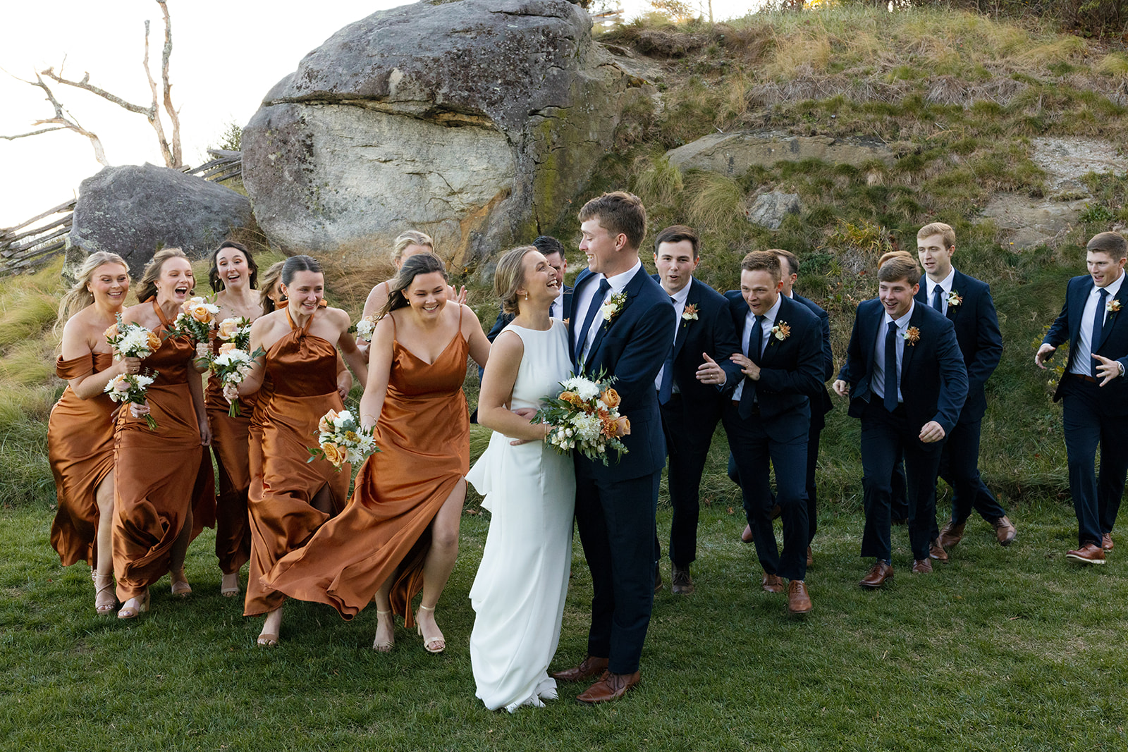 Bridesmaids and groomsmen run joyfully toward the newlyweds in a playful outdoor photo.
