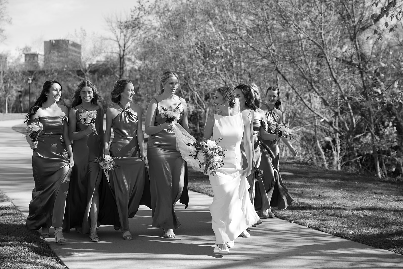 Bride laughs with her bridesmaids as they walk together in flowing dresses before the romantic ceremony at glassy chapel.