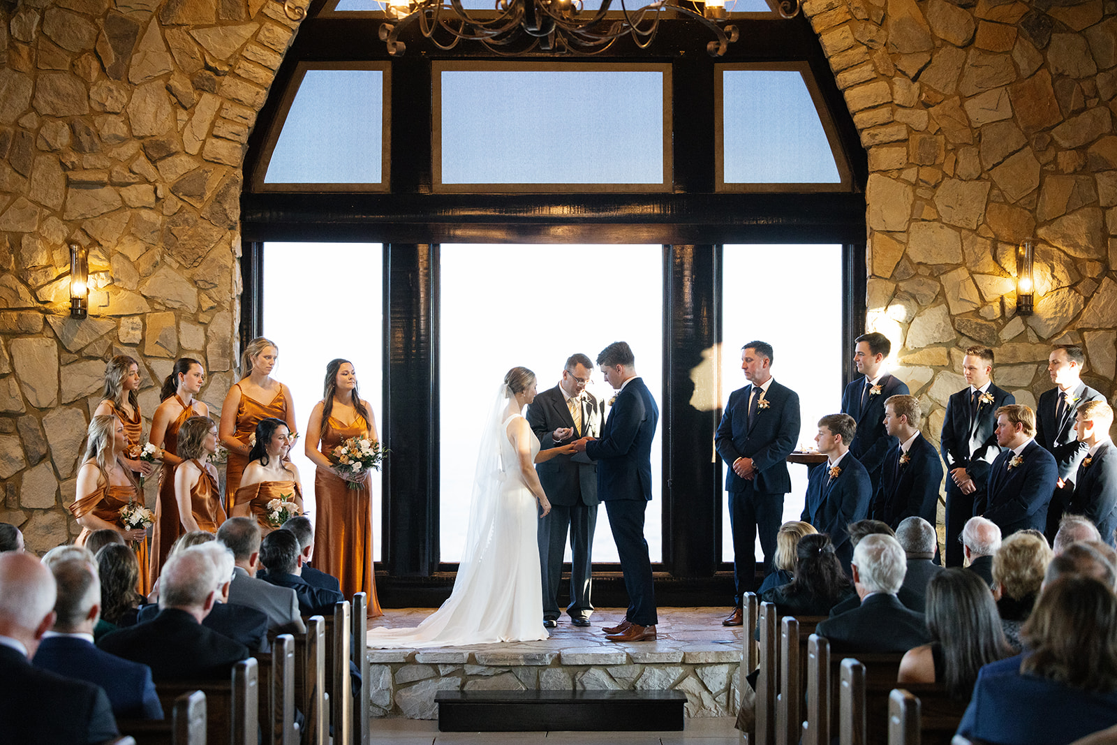 Groom places the wedding ring on his partner’s finger during their heartfelt vow exchange at glassy chapel.