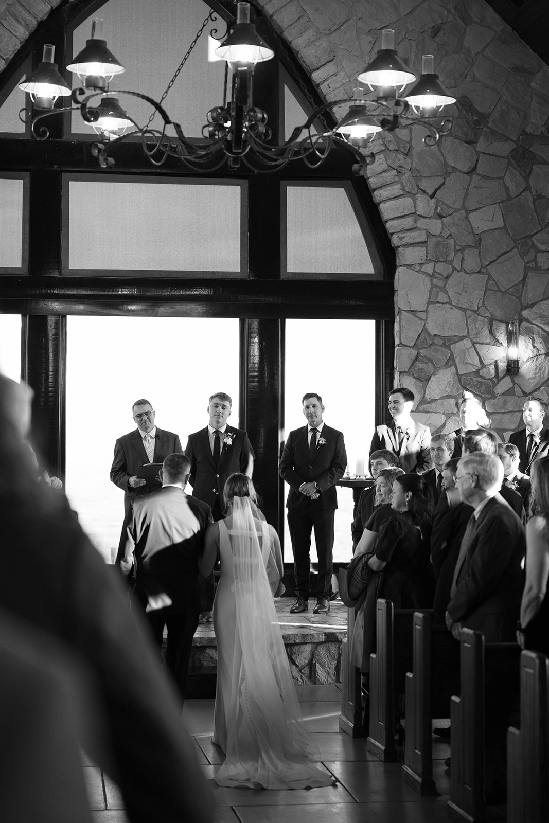 The groom watches tenderly as the bride is escorted down the aisle in a sunlit Cliffs at Glassy Chapel.